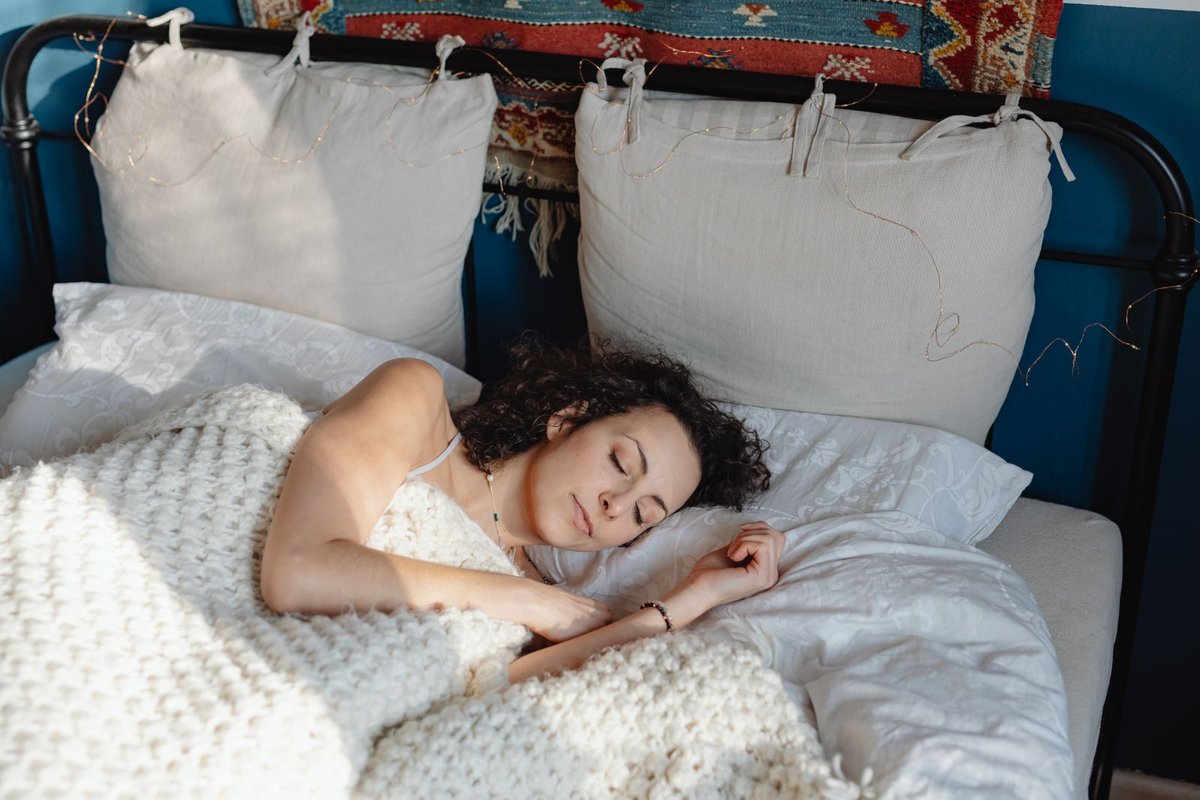 perimenopause-sleep-tips-woman-sleeping Woman with dark curly hair sleeping peacefully under a cream knit blanket